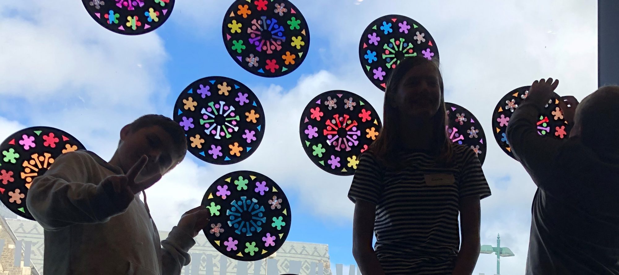 Children beside a window covered in colourful paper rose-window designs